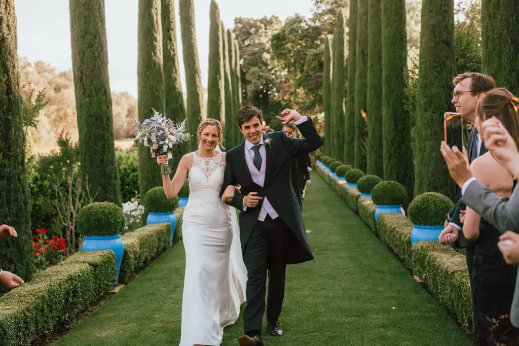 Novios recién casados caminando entre cipreses, la novia con un ramo silvestre en tonos lila
