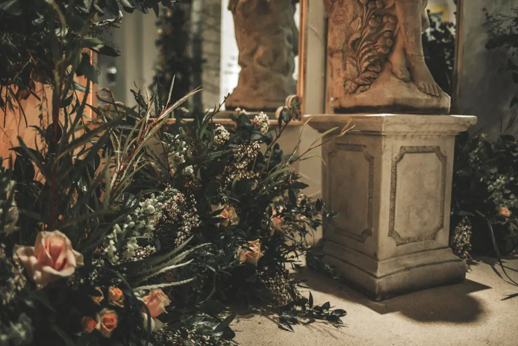 Decoración con follaje y rosas color melocotón junto a un pedestal de piedra