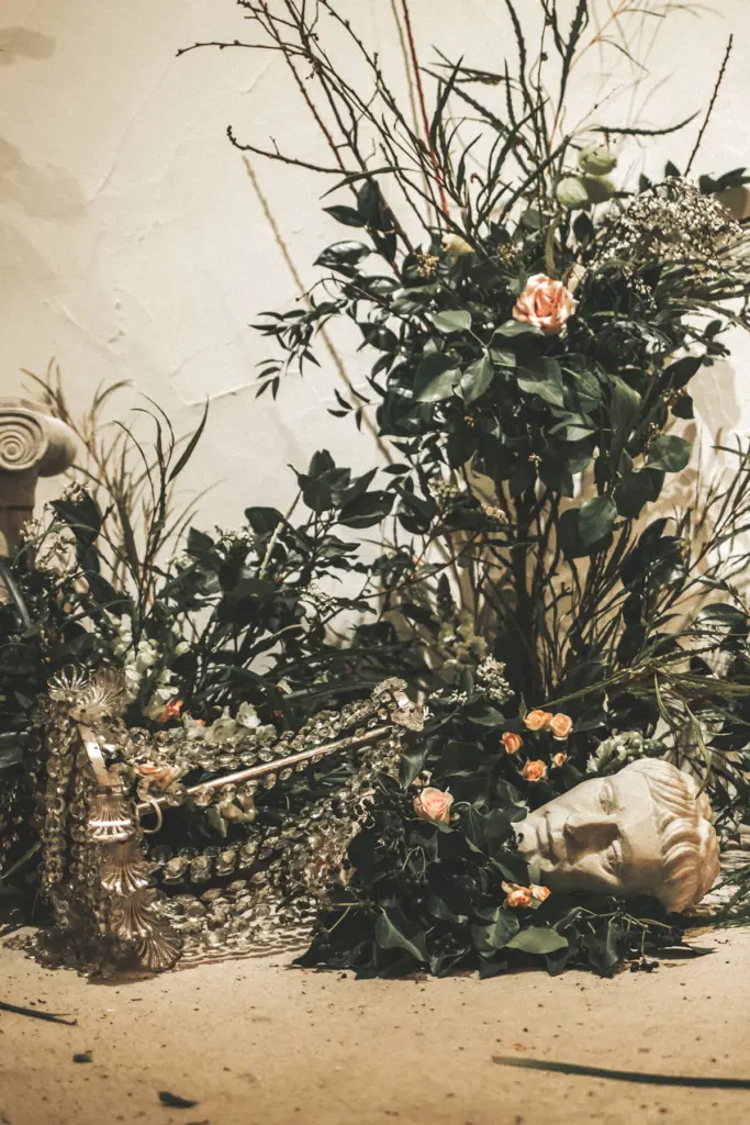 Arreglo de rosas melocotón y follaje con objetos decorativos dorados