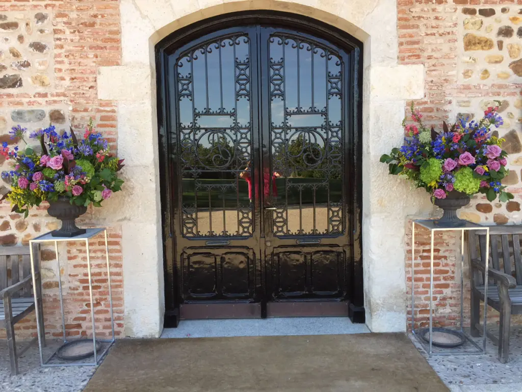 Entrada con puerta de forja flanqueada por dos arreglos florales en copas