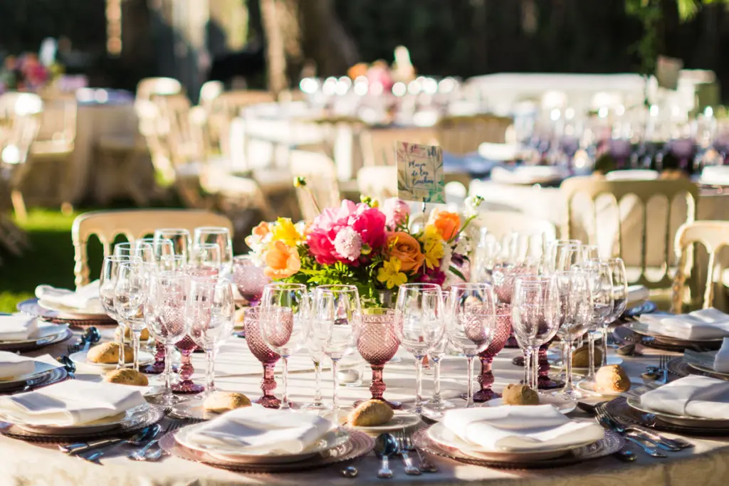 Centro de mesa de colores vivos entre copas rosas en un banquete al aire libre