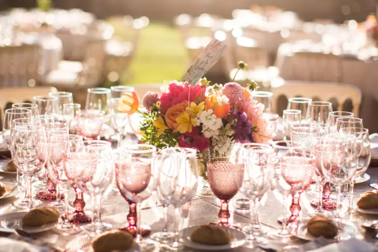 Centro de mesa de dalias y rosas en tonos coral y naranja entre copas de cristal rosa