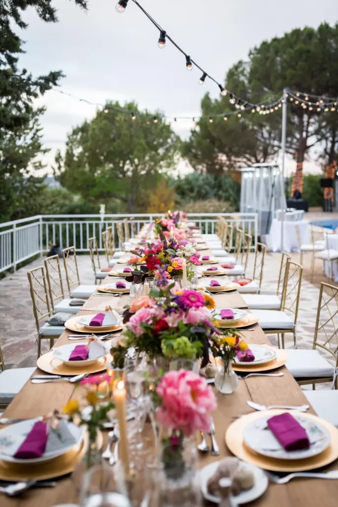 Mesa imperial en una terraza con centros de flores de colores y bajoplatos dorados