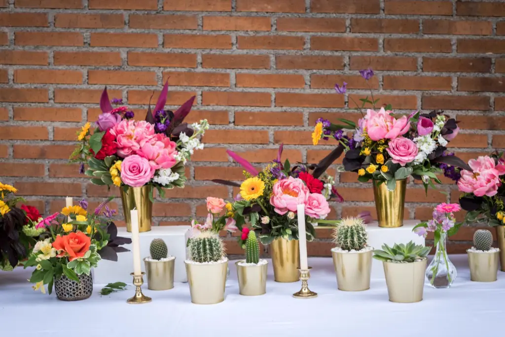 Jarrones dorados con peonías y dalias de colores y cactus sobre un fondo de ladrillo