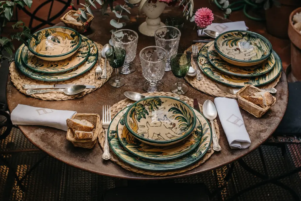 Detalle de una mesa con vajilla de cerámica verde y amarilla y copas talladas