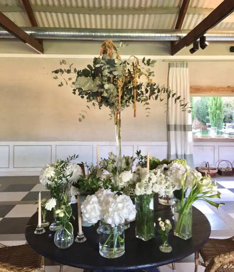 Mesa con jarrones de cristal con hortensias y calas blancas y ramas altas